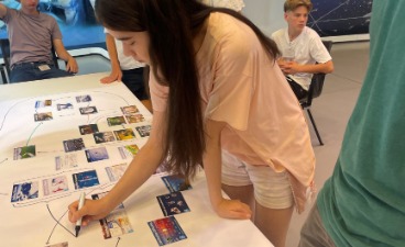 Eine Jugendliche beschriftet und ordnet Infokarten auf einem großen Tischplakat zum Thema Klimawandel und CO2-Emissionen.