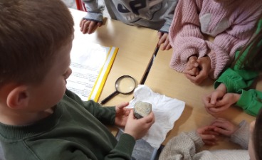 Kinder sitzen um einen Tisch und untersuchen aufmerksam einen Stein mit einer Lupe.