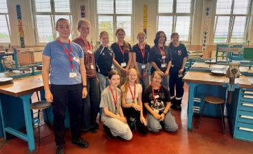 Die zehn Teilnehmerinnen des Mädchen für Technik-Camps stehen und knien für ein Gruppenbild in einer Ausbildungswerkstatt der ZF in Schweinfurt. Sie tragen Namensschilder und lächeln.