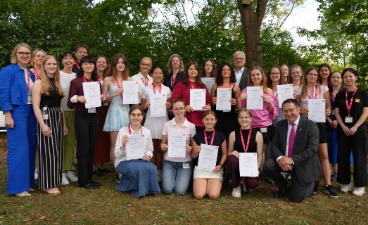 Eine Gruppe von Erwachsenen und jungen Frauen posieren mit Urkunden für ein Foto.